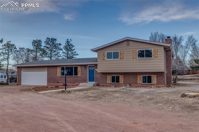 split level home with a garage, dirt driveway, a chimney, and brick siding