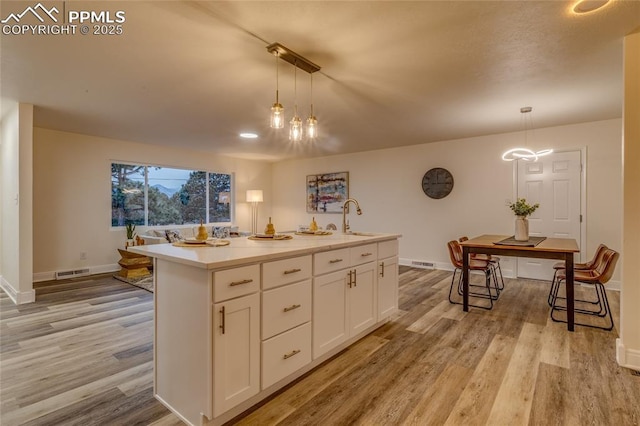 kitchen featuring hanging light fixtures, light wood-style floors, white cabinetry, and visible vents