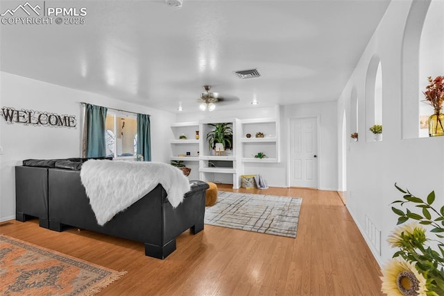 living room featuring built in features, visible vents, baseboards, and wood finished floors