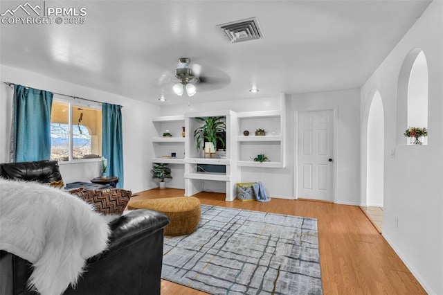 living room featuring arched walkways, visible vents, a ceiling fan, wood finished floors, and baseboards