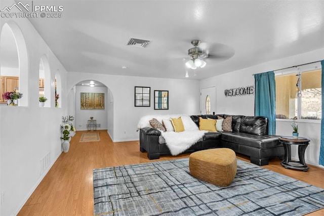 living room featuring ceiling fan, light wood-style flooring, visible vents, and arched walkways