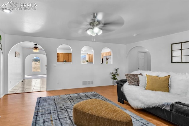 living area with light wood-type flooring, arched walkways, visible vents, and a ceiling fan