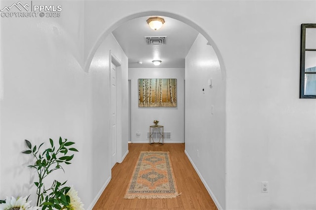 hallway featuring baseboards, visible vents, arched walkways, and wood finished floors