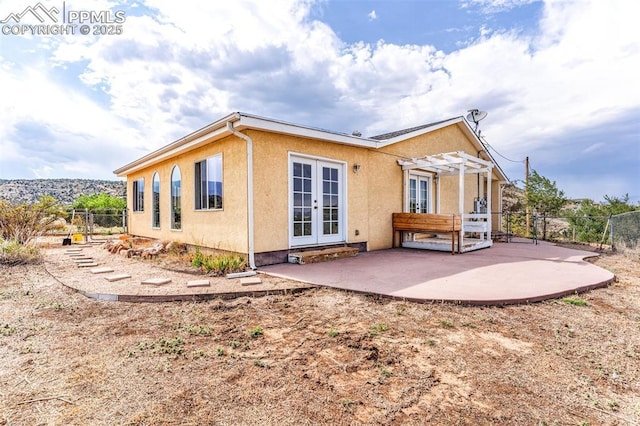 rear view of property with french doors, stucco siding, a patio area, fence, and a pergola