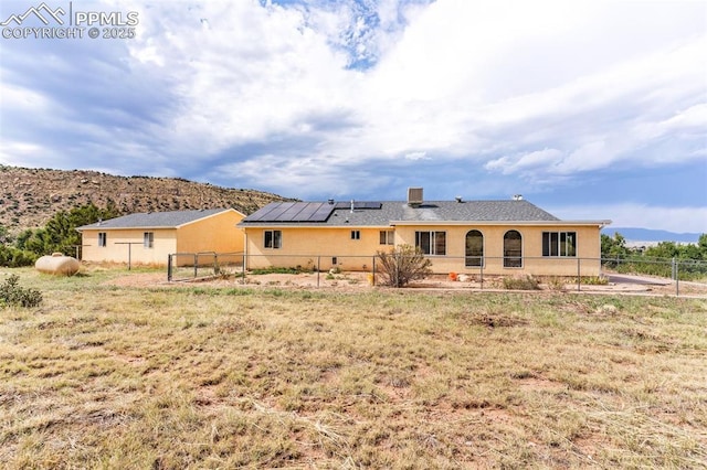 back of house with fence, a mountain view, solar panels, and stucco siding