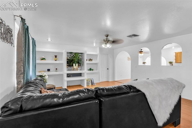 living area with built in shelves, arched walkways, visible vents, light wood-style flooring, and a ceiling fan