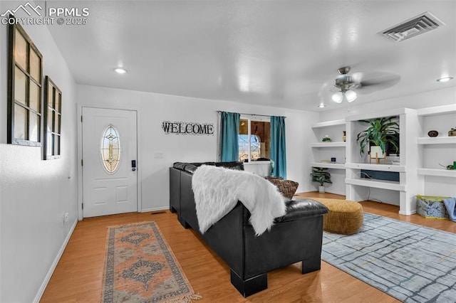 living room with ceiling fan, built in shelves, wood finished floors, visible vents, and baseboards