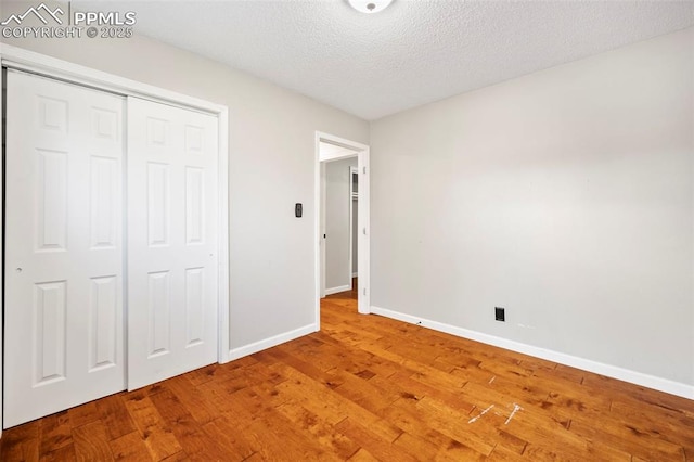 unfurnished bedroom featuring a closet, baseboards, light wood-style flooring, and a textured ceiling