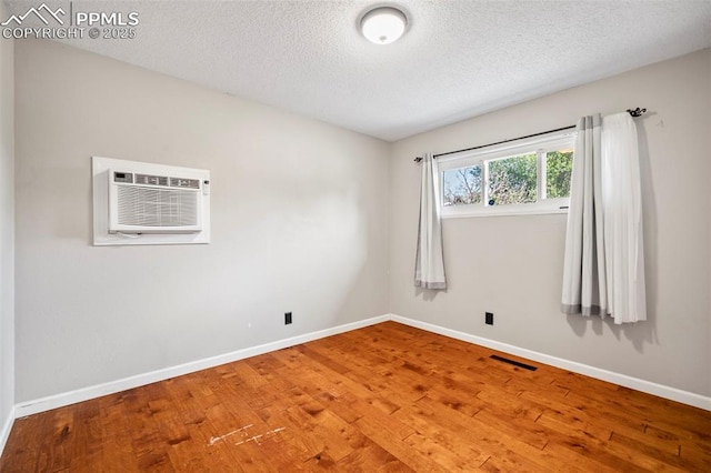 unfurnished room with baseboards, hardwood / wood-style floors, and an AC wall unit