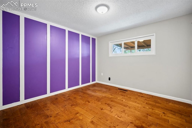 unfurnished room featuring baseboards, a textured ceiling, visible vents, and hardwood / wood-style floors