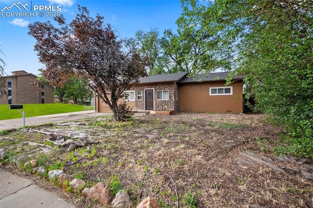 ranch-style house featuring driveway, stone siding, and a front lawn