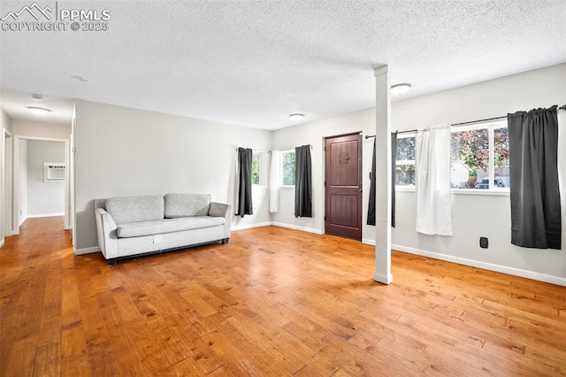 living area featuring wood-type flooring, baseboards, a textured ceiling, and a wall mounted AC