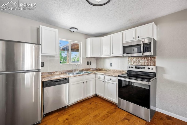 kitchen featuring stainless steel appliances, white cabinetry, a sink, and hardwood / wood-style floors