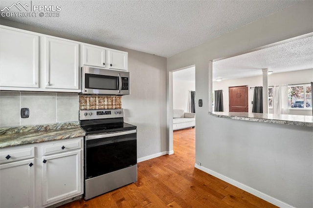 kitchen featuring stainless steel appliances, white cabinets, a textured ceiling, wood finished floors, and baseboards