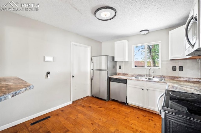 kitchen with visible vents, white cabinets, stainless steel appliances, light wood-type flooring, and a sink