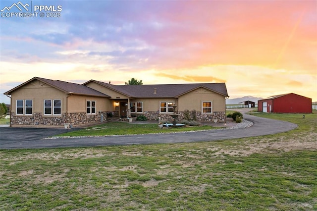 back of property featuring stone siding, a lawn, driveway, and stucco siding