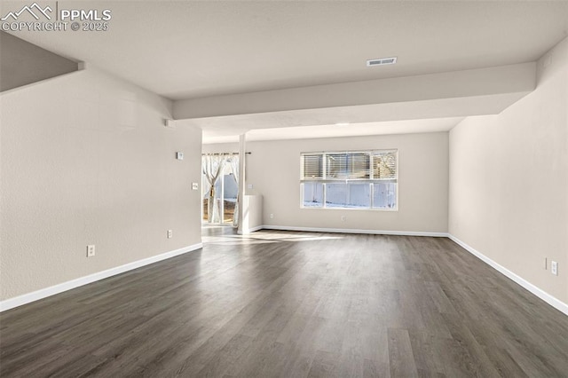 empty room with dark wood-style flooring, visible vents, and baseboards