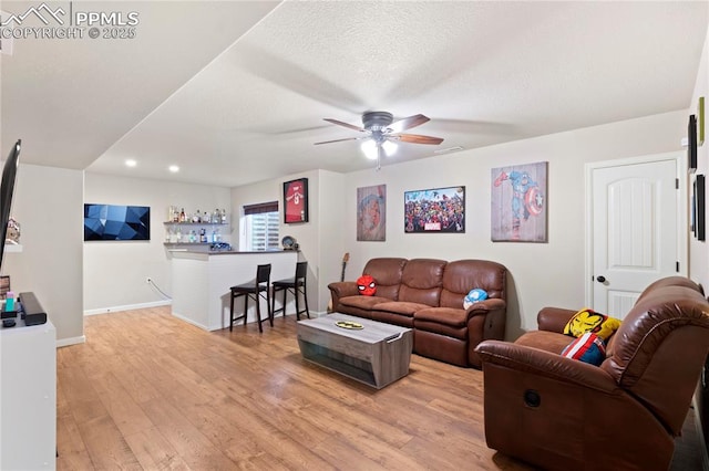 living area with a dry bar, light wood-style floors, ceiling fan, a textured ceiling, and baseboards