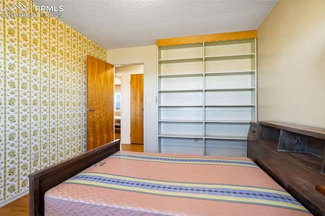 bedroom featuring a textured ceiling, baseboards, wood finished floors, and wallpapered walls