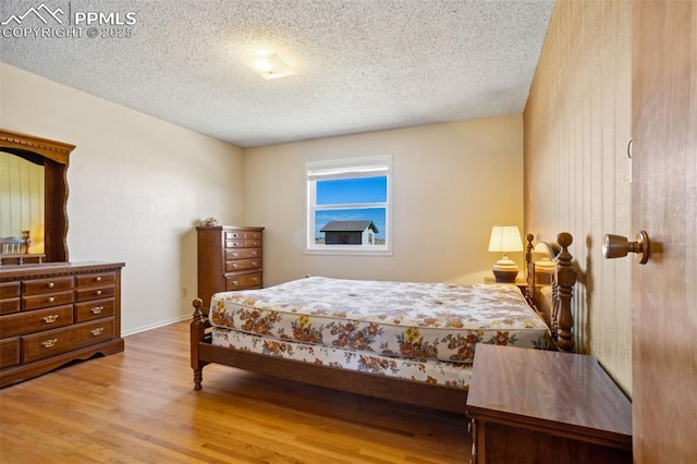 bedroom with light wood-style floors, a textured ceiling, and baseboards