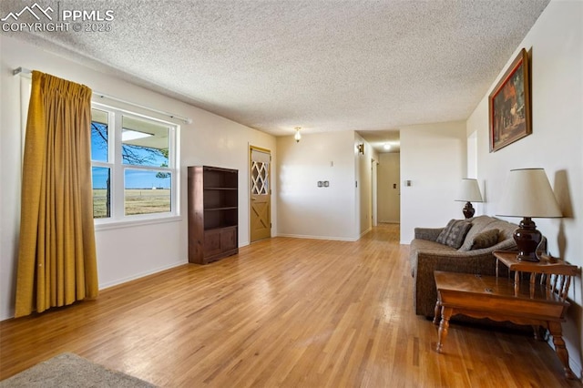 living area with baseboards, a textured ceiling, and light wood finished floors