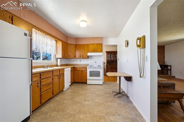 kitchen with white appliances, brown cabinetry, light countertops, under cabinet range hood, and a sink