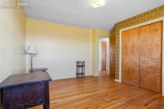 bedroom with a closet, a textured ceiling, baseboards, and wood finished floors