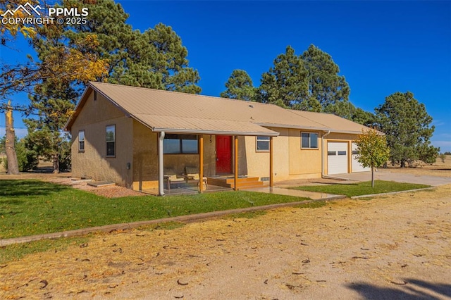 back of property featuring a yard, stucco siding, an attached garage, metal roof, and driveway