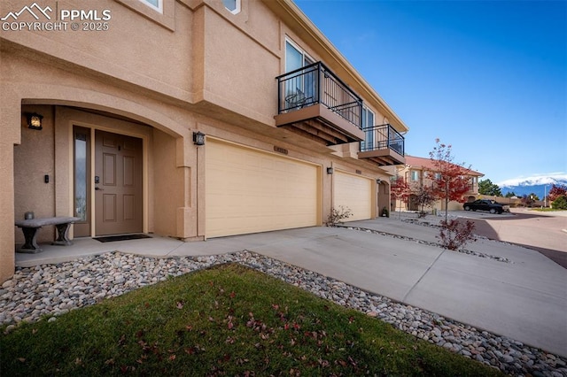 view of side of property with a garage, concrete driveway, a balcony, and stucco siding