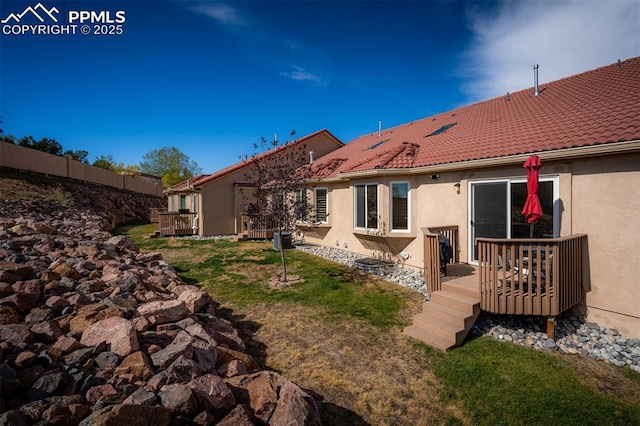 back of property featuring a tiled roof, a lawn, a wooden deck, and stucco siding