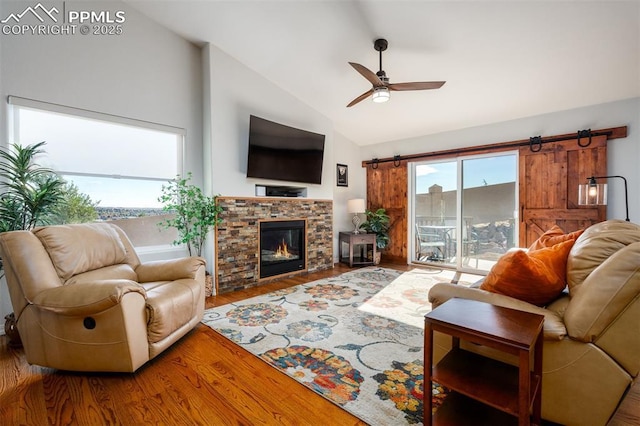 living room with ceiling fan, a barn door, wood finished floors, vaulted ceiling, and a glass covered fireplace