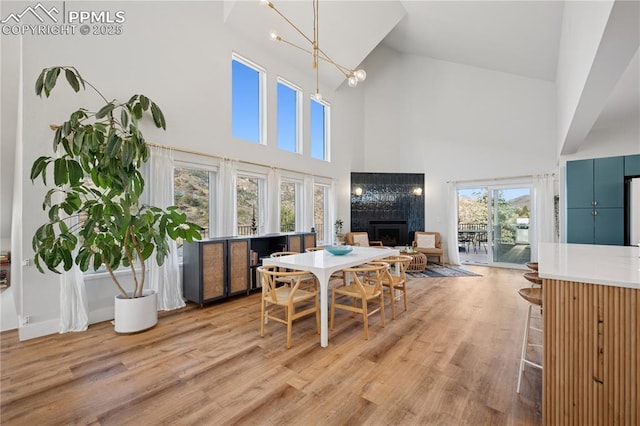 dining space featuring a tile fireplace, a notable chandelier, light wood-style flooring, and a towering ceiling