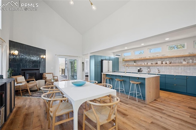 dining space featuring high vaulted ceiling, a fireplace, and light wood-style floors