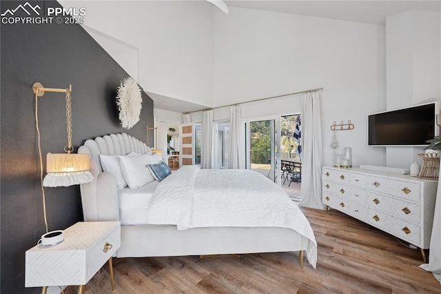 bedroom featuring wood finished floors, a towering ceiling, and access to exterior