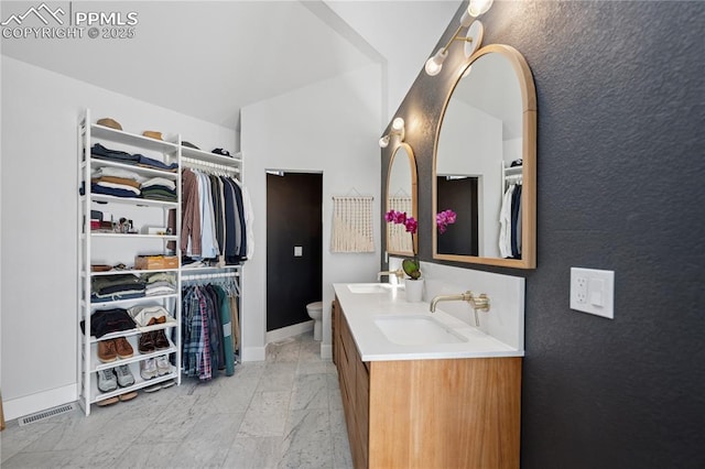 bathroom with marble finish floor, double vanity, a spacious closet, and a sink