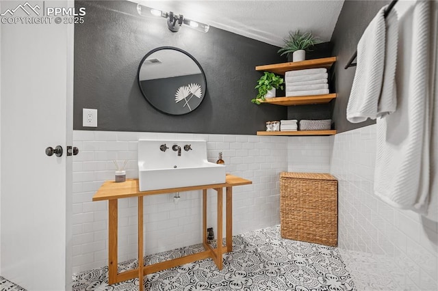 bathroom featuring a wainscoted wall, tile walls, a sink, a textured ceiling, and tile patterned floors