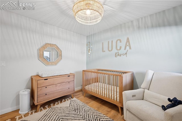 bedroom with a nursery area, an inviting chandelier, baseboards, and wood finished floors