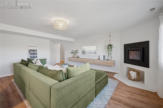 living room with a fireplace with flush hearth, visible vents, and wood finished floors