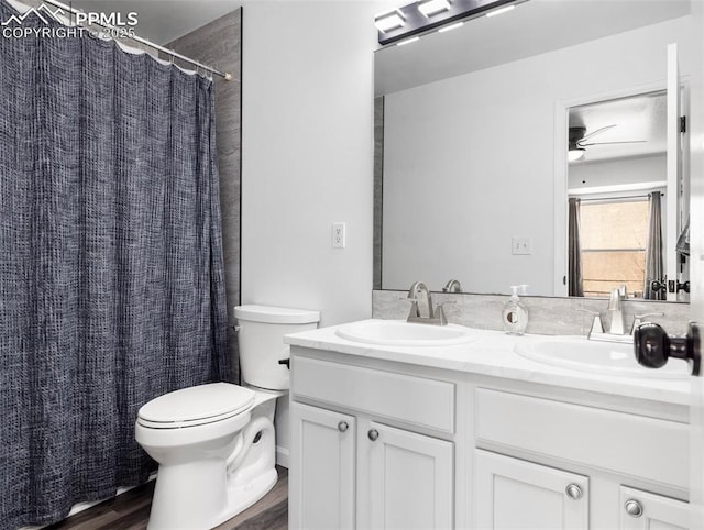 bathroom featuring toilet, double vanity, a sink, and wood finished floors