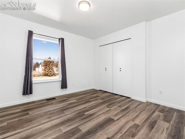 unfurnished bedroom with a closet, visible vents, baseboards, and wood finished floors