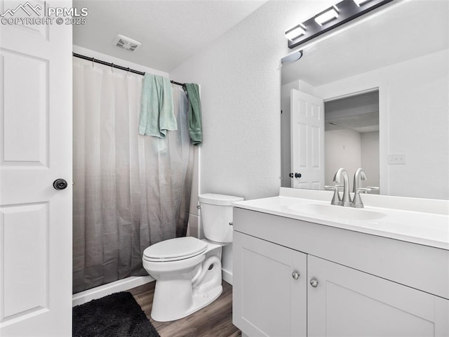 full bathroom with visible vents, a textured wall, toilet, wood finished floors, and vanity