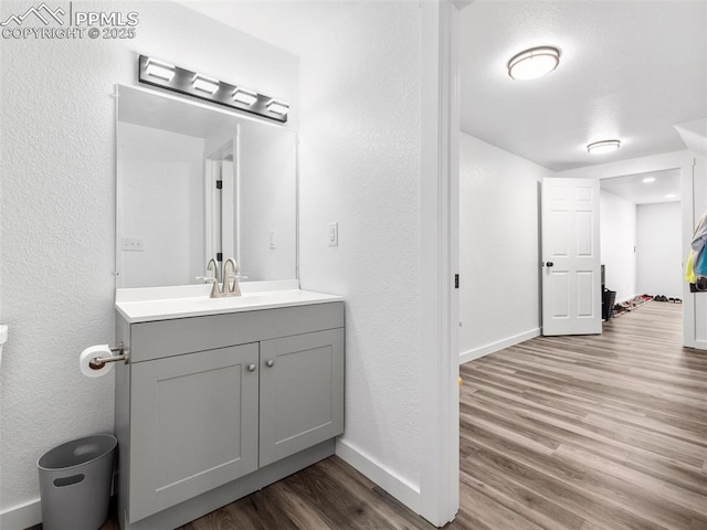 bathroom with a textured wall, wood finished floors, vanity, and baseboards