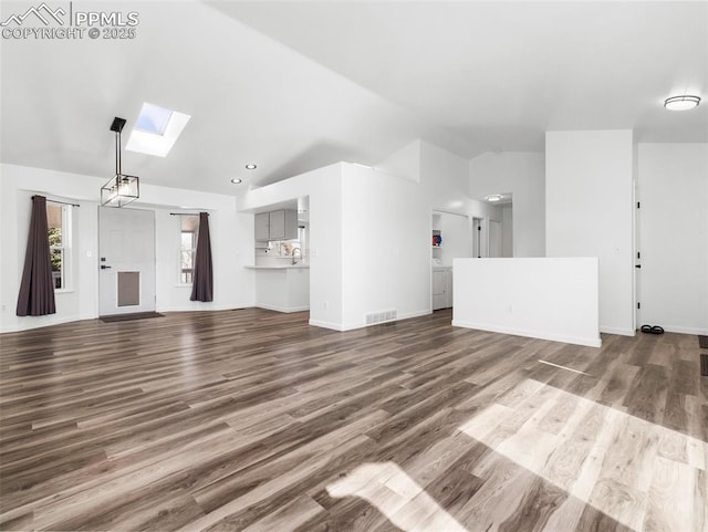 unfurnished living room with vaulted ceiling with skylight, wood finished floors, visible vents, and baseboards