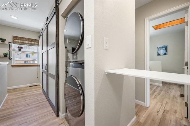 interior space with stacked washing maching and dryer, a barn door, baseboards, and light wood finished floors