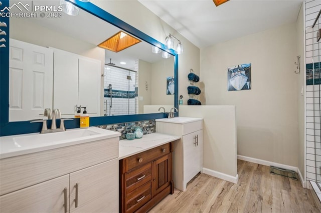 bathroom featuring a skylight, wood finished floors, vanity, baseboards, and a stall shower