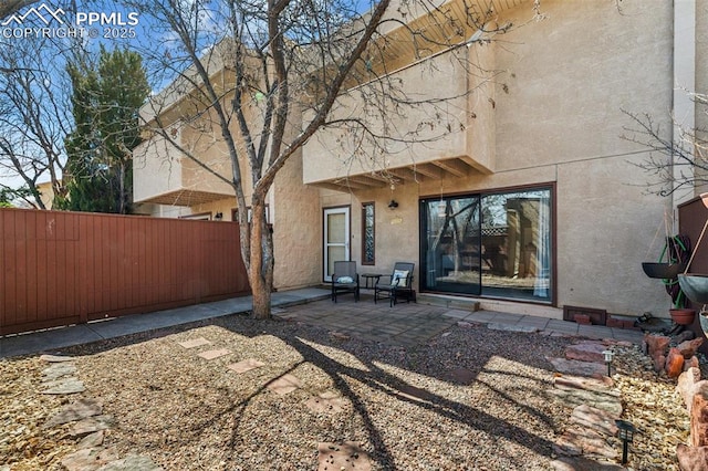 rear view of property featuring a patio area, fence, and stucco siding