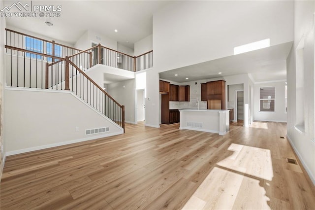 unfurnished living room with light wood-type flooring, visible vents, baseboards, and stairs