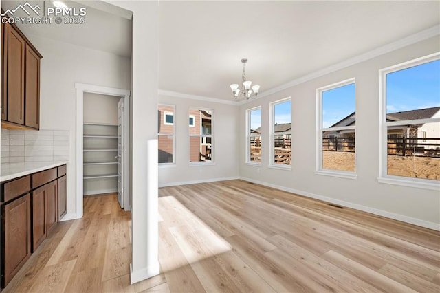 unfurnished dining area with light wood-style floors, crown molding, baseboards, and an inviting chandelier