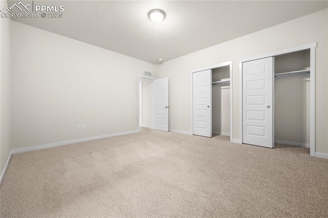 unfurnished bedroom featuring a textured ceiling, carpet floors, visible vents, baseboards, and two closets