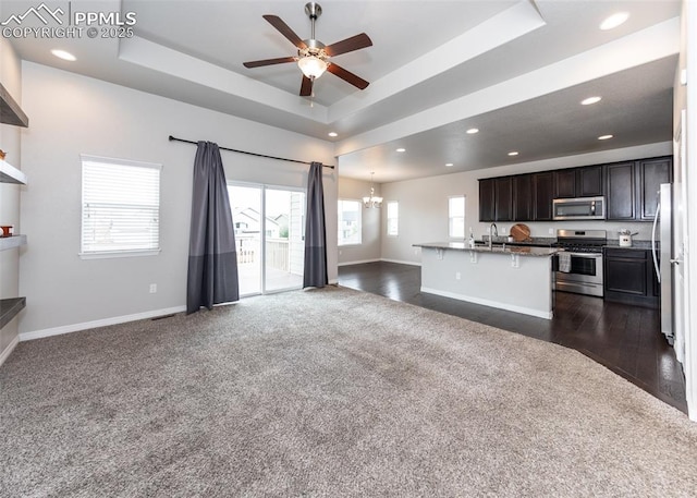 unfurnished living room featuring dark colored carpet, recessed lighting, a raised ceiling, baseboards, and ceiling fan with notable chandelier